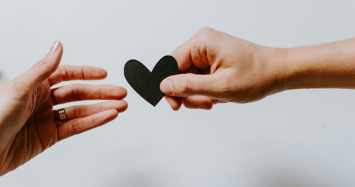 person reaching black heart cutout paper